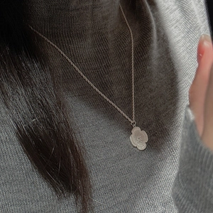 Macro detail of a vintage S925 silver flower pendant necklace on a grey turtleneck sweater