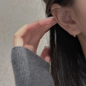 Close-up of a small golden vintage textured hoop earring on ear with braided details