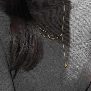 Detailed view of a gold Y-shaped lariat necklace with a small bead on a grey sweater