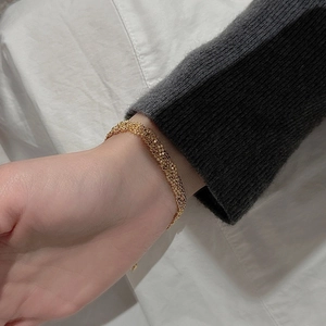 Détail d'un bracelet tissé doré au poignet avec fond en pull en tricot gris foncé