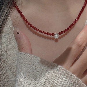 Detail of red beaded necklace with silver textured pendant on beige sweater
