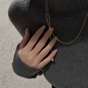 Detail of a minimalist gold Y-shaped necklace with sliding ring and sphere pendant on a model