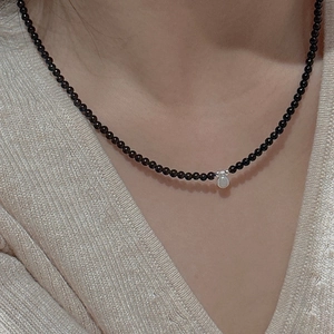 Minimalist black beaded necklace with a silver teardrop pendant worn on the neck