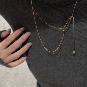 Detail of a minimalist gold spherical pendant on a fine silver chain over grey knitwear