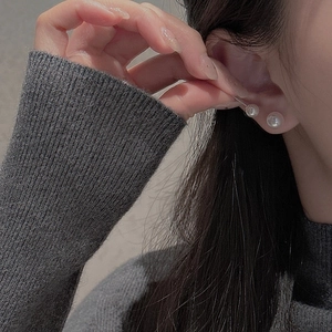 Close-up of elegant double pearl stud earrings worn by a model on a gray knit top