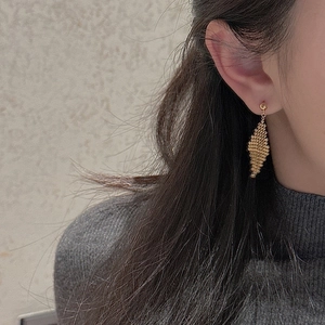 Close-up of vintage golden rhombus beaded tassel earrings worn by a model in a cozy setting