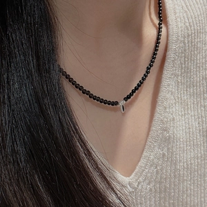 Close-up of minimalist black beaded necklace with a silver teardrop pendant on neck