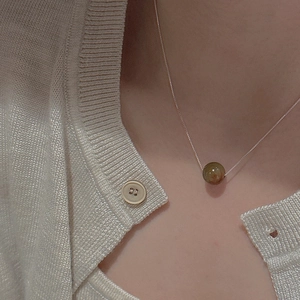 Macro detail of a minimalist silver chain with a polished round green stone pendant