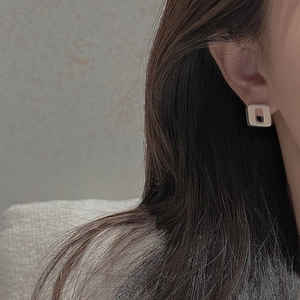 Detailed view of square geometric silver stud earrings worn on a female model's ear