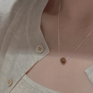 Gros plan d'un collier en argent minimaliste avec une perle de pierre brune sur un modèle