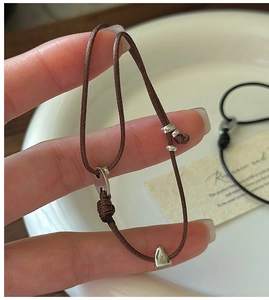 Détail du bracelet en cuir tressé ajustable avec breloque cœur en argent et nœud coulant