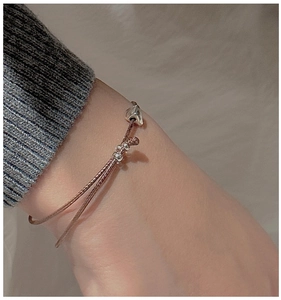Détail du pendentif cœur sur bracelet en cordon marron foncé porté au poignet