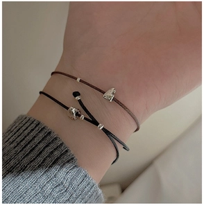 Gros plan de bracelets cordons minimalistes noir et marron avec breloques argentées