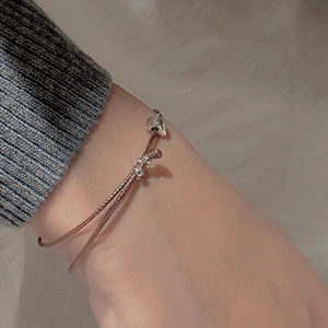 Bracelet en corde tressée marron avec breloque cœur en argent S925 porté sur un pull gris