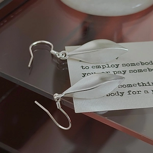 Minimalist S925 sterling silver leaf drop earrings with a matte brushed finish on a glass stand