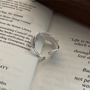 Minimalist S925 sterling silver feather ring with adjustable open design on a book