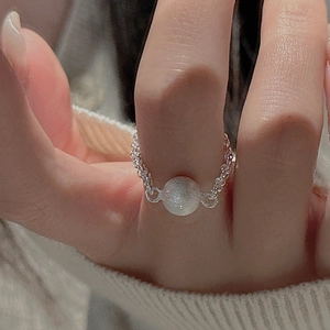 Detail of silver chain ring with brushed bead on finger against white knit fabric