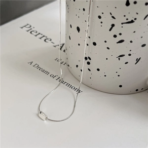 Close-up of a minimalist silver square pendant necklace resting on a ceramic cup