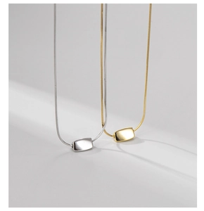 Close-up of gold and silver square bean pendants on delicate snake chain necklaces