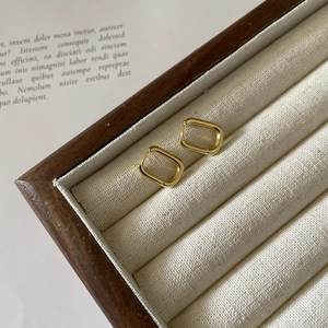 Pair of minimalist gold U-shaped silver earrings displayed on a rustic wooden jewelry tray