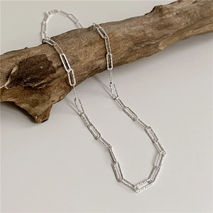 Detailed macro view of silver S925 paperclip chain with unique hammered texture on wood