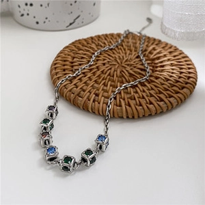 Détail d'un collier argenté vintage avec pendentifs en pierres colorées sur support rotin