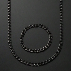 All-black stainless steel Cuban link chain necklace and bracelet set on dark background