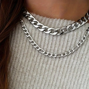 Layered silver stainless steel curb and figaro chain necklaces on a white knit sweater