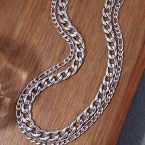 Polished silver stainless steel curb and figaro chain necklaces on a wood background