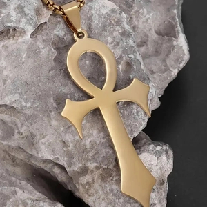 Detailed close-up of golden Ankh cross pendant with matte finish on a natural grey rock