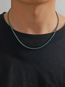 Détail d'un collier chaîne fin en acier inoxydable sarcelle porté sur un t-shirt noir