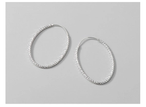 Macro detail of diamond-cut textured silver oval hoop earrings with shimmering surface