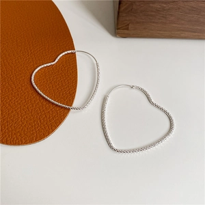 Macro detail of S925 sterling silver heart hoop earrings with sparkling diamond cut texture