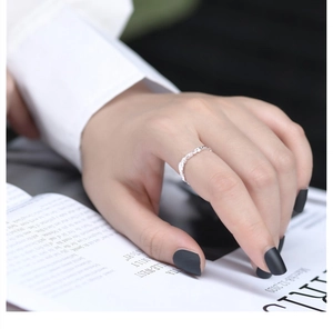 Macro detail of a minimalist silver wavy textured ring styled on a hand with a white shirt