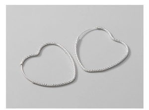 Macro detail of large S925 silver heart hoop earrings with shimmering textured finish
