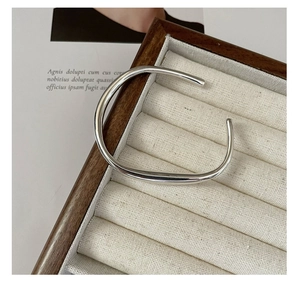 Close-up of polished silver liquid-style open ring on a wooden jewelry display stand