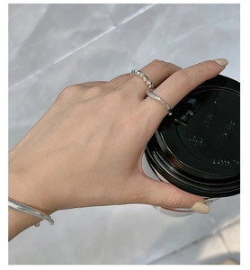 Irregular liquid silver rings and slim bracelet shown on a hand holding a coffee cup