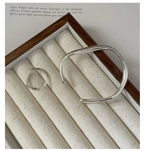 Detailed view of irregular fluid silver ring and bangle set on beige jewelry display