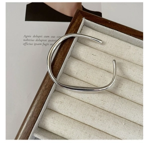 Macro view of the irregular liquid-wave silver bangle on a dark wood display tray