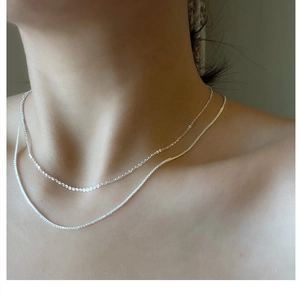 Detail of layered S925 sterling silver Chopin chain necklaces worn on a model's neck