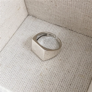 Détail d'une bague carrée en argent sterling S925 poli sur fond beige texturé