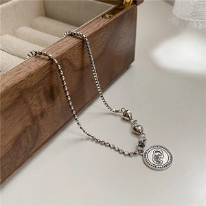 Detailed view of retro elephant coin and heart charms on asymmetric silver chain