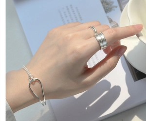 Detail of silver knot bracelet and rings set with textured metal finish on white books