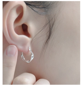 Gros plan de boucles d'oreilles créoles torsadées en argent sterling S925 sur l'oreille
