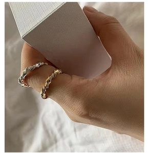 Detail of twisted S925 sterling silver rings in gold and silver on a finger