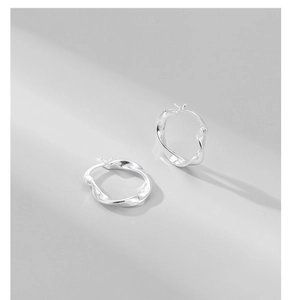 Détail macro de créoles torsadées en argent sterling S925 avec design poli ondulé