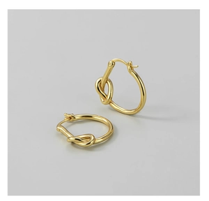 Vue détaillée de boucles d'oreilles nœud dorées polies au design minimaliste sur fond gris