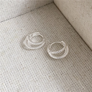 Detail of S925 sterling silver twist double-layer hoop earrings on textured fabric