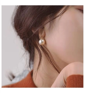 Detail of a 10-12mm white pearl earring with gold hook on a model wearing orange knitwear