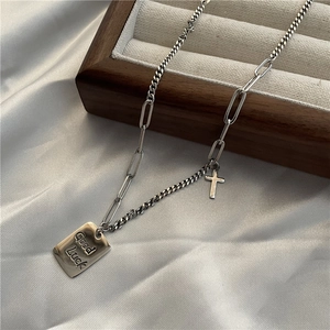 Macro detail of silver S925 Good Luck square tag and cross charms on a vintage chain